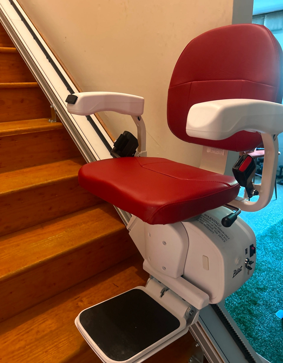 a new stairlift with red chair covers about to climb a wooden stairway
